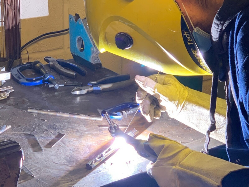 A close up image of a person in a welding mask using a blowtorch to heat and shape metal